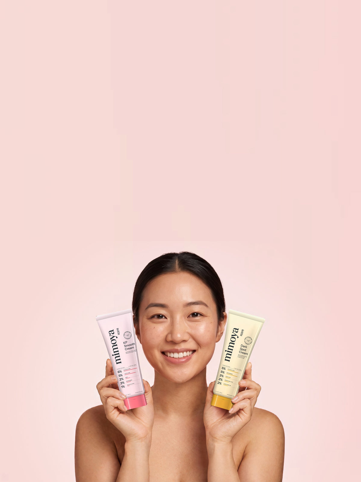 Smiling woman holding MIMOYA KP Smooth Cream for keratosis pilaris and MIMOYA Dark Spot Cream for hyperpigmentation